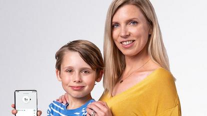 Woman wearing a yellow blouse standing next to a young boy holding up a dexcom receiver
